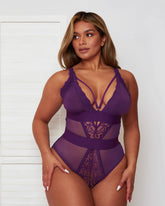 Model wearing the Alicia Fuller Bust Curvy Girl Bodysuit in Purple, featuring a plunging neckline with strappy detailing, lace-trimmed cups, sheer mesh panelling, and a sculpting high-waisted silhouette designed for fuller bust support.
