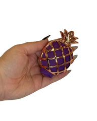 Hand holding a pineapple-shaped object with purple and gold design on a white background