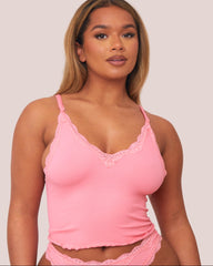 Woman wearing a pink lace-trimmed camisole against a plain background