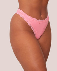 Pink lace thong worn by a person on a plain background