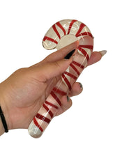 Glass candy cane with red and white stripes held by a hand on a white background