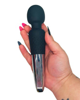 Hand holding a black and silver personal massager adult toy against a white background