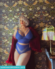 Statue of a woman in a blue lingerie set with a red cape against a patterned wall.