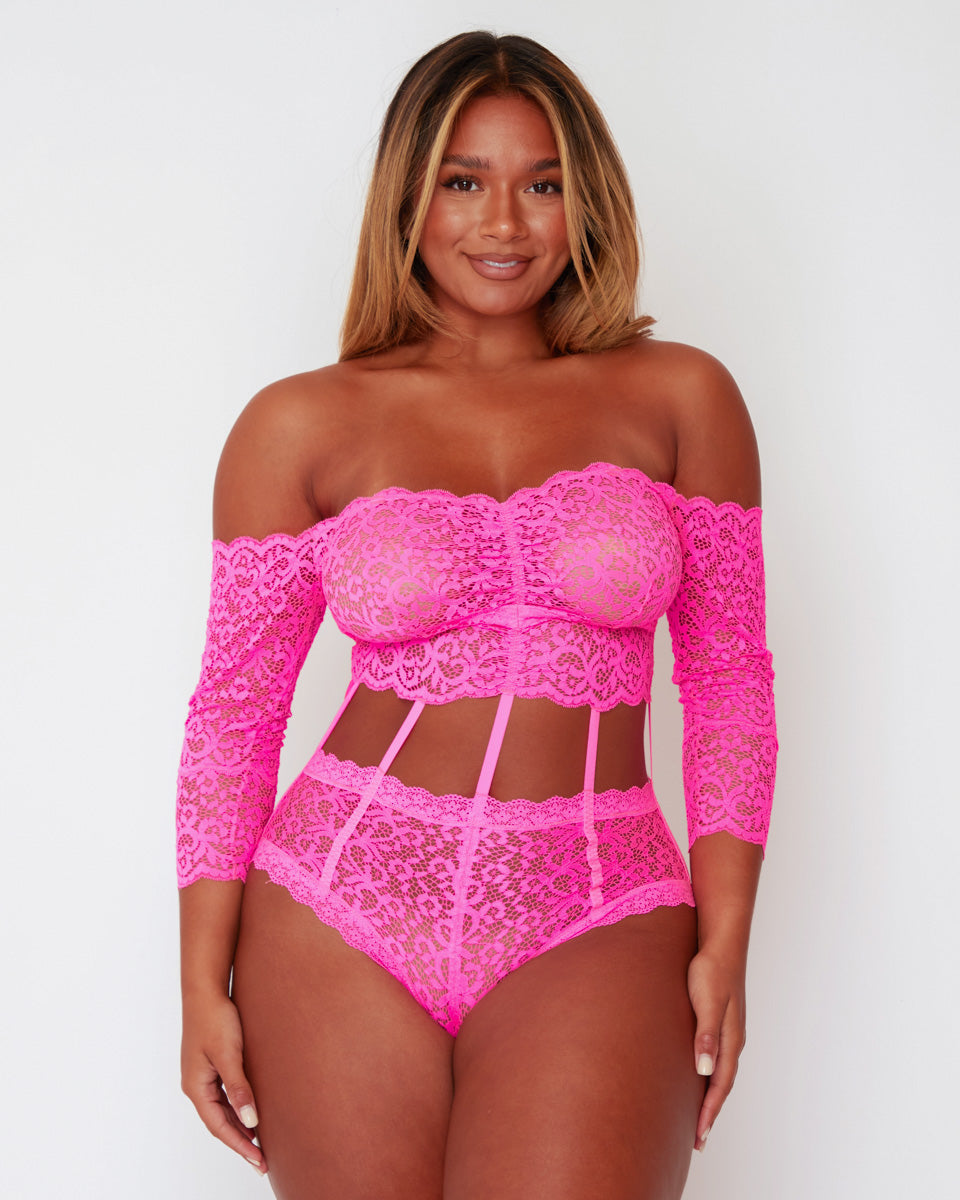 Full front view of the Alix Bodysuit in Pink, featuring a bandeau-inspired lace bust, long lace sleeves, decorative waist straps, and a high-leg fit designed to enhance curves.