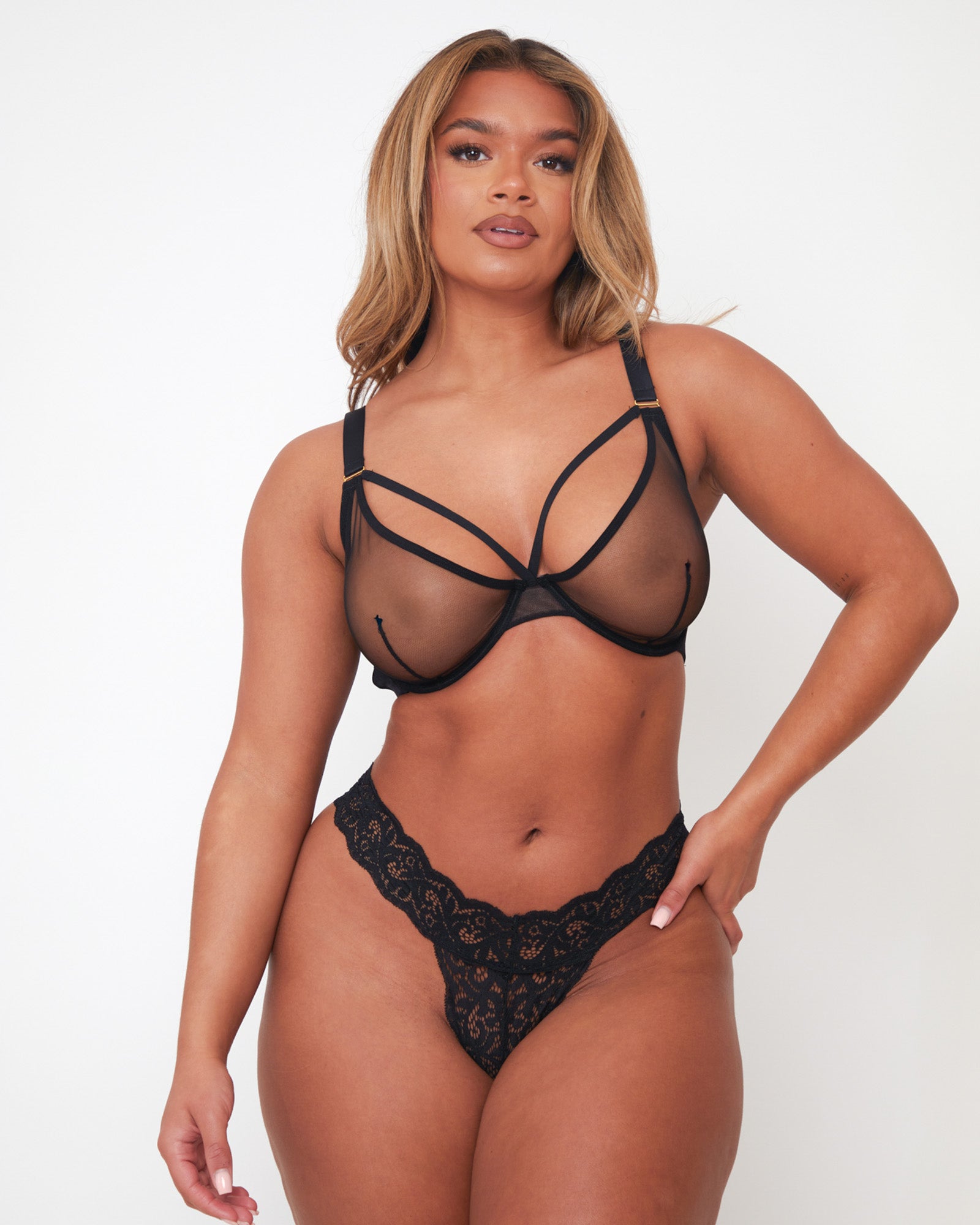 Model wearing Tutti Rouge Carina black sheer mesh underwired bra with strappy neckline, paired with a black lace thong.