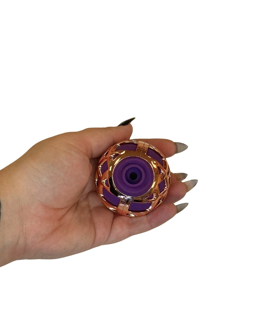 Hand holding a small purple and gold object against a white background