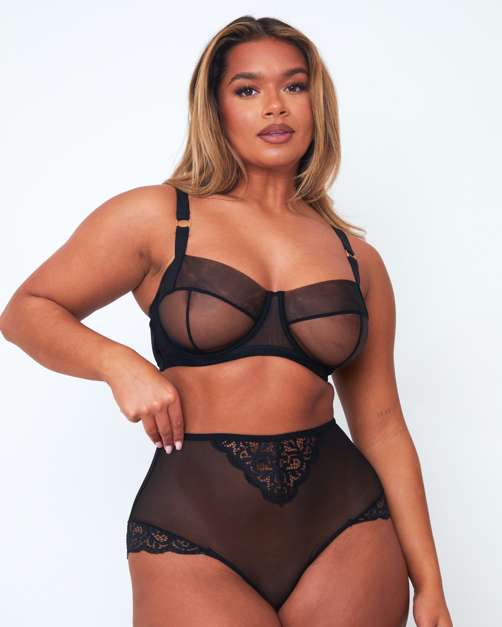 Angled view of Tutti Rouge Raya black sheer mesh bra on a model, showing seamed cups and underwiring, paired with lace-trimmed briefs.