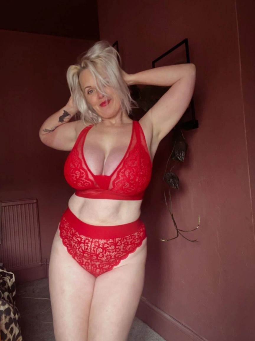 Woman wearing a red lace lingerie set against a maroon wall.