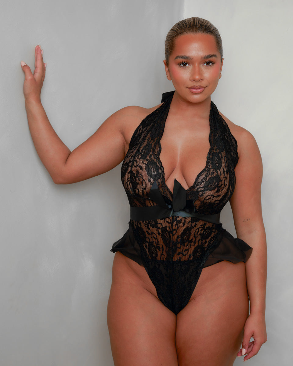 Front view of the Tutti Boudoir Imani Teddy in Onyx Black, showcasing the deep plunge lace cups, elegant satin bow waistband and feminine mesh frill accents for a seductive silhouette.